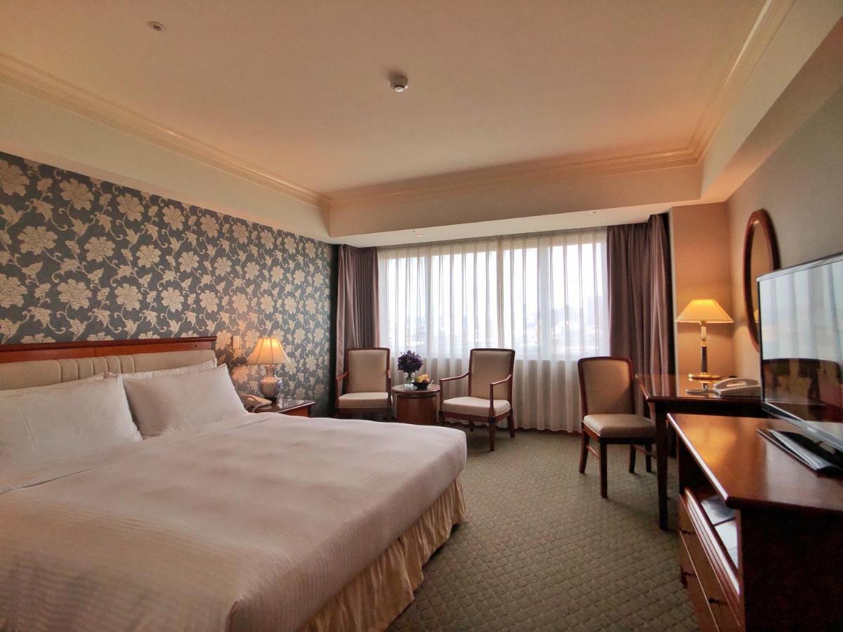 Evergreen Laurel Hotel - Tchaj-čung Exteriér fotografie The photo shows a well-appointed hotel room. It features a large bed with white bedding and a decorative headboard. The walls are adorned with a patterned wallpaper, possibly floral, adding a touch of elegance. There is a window with sheer curtains t