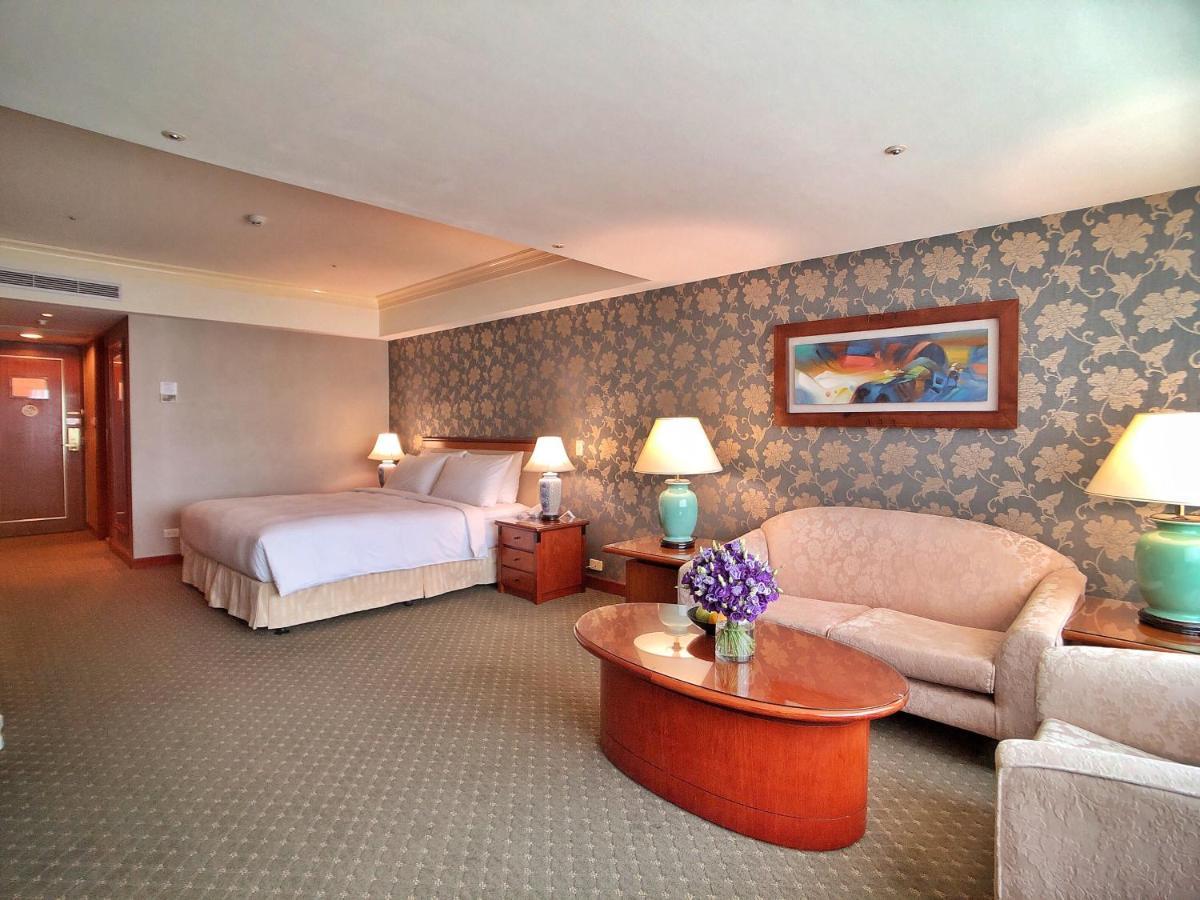Evergreen Laurel Hotel - Tchaj-čung Exteriér fotografie The photo shows a hotel room that features a well-furnished space. It includes a large bed with a light-colored bedspread, a comfortable sofa, and armchair. There's a coffee table with a vase of flowers in the center. The room has a decorative wallpa