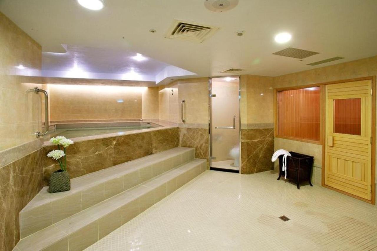 Evergreen Laurel Hotel - Tchaj-čung Exteriér fotografie The photo shows a spacious and well-lit spa or wellness area. It features a large, recessed hot tub with steps leading up to it, surrounded by beige marble walls. There's a shower area enclosed in glass, and to the right, a wooden sauna or steam room