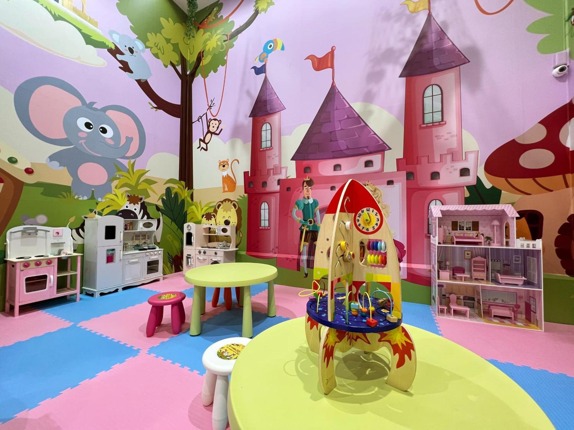 Evergreen Laurel Hotel - Tchaj-čung Exteriér fotografie The photo shows a colorful children's playroom designed with a whimsical theme. The walls are painted in bright colors and feature a cartoon-style mural of a pink castle with purple towers and a smiling cartoon elephant. The room is filled with playf
