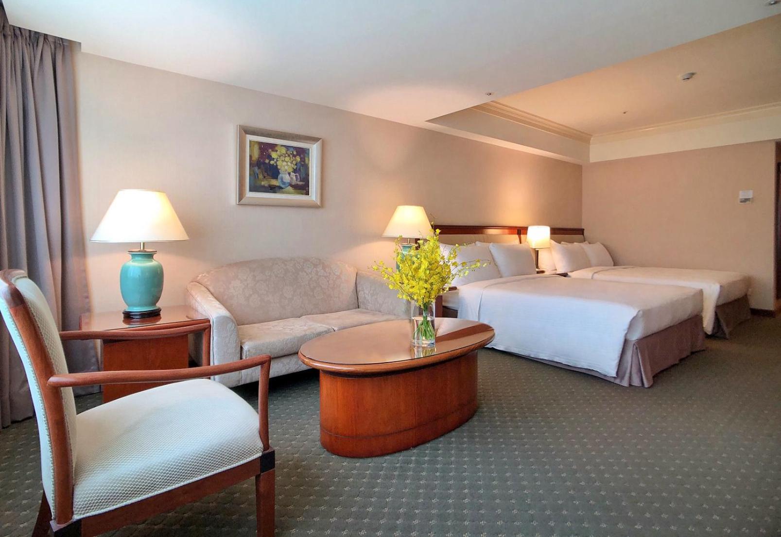 Evergreen Laurel Hotel - Tchaj-čung Exteriér fotografie The photo shows a hotel room featuring two beds, a small seating area, and a coffee table. The walls are painted in soft, neutral colors, and there is a framed piece of artwork hanging on the wall. A potted plant with yellow flowers is placed on the 