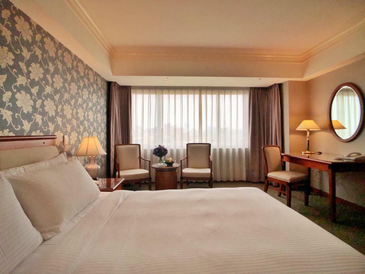 Evergreen Laurel Hotel - Tchaj-čung Exteriér fotografie The photo shows a hotel room with a comfortable and inviting design. There is a large bed with crisp white bedding on the left side of the image. To the right, there are two elegant chairs with a small round table between them, adorned with a bouquet