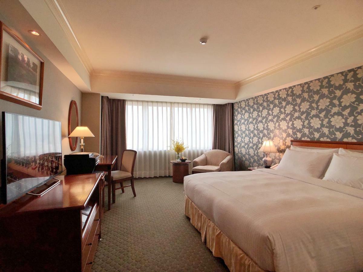 Evergreen Laurel Hotel - Tchaj-čung Exteriér fotografie The photo shows a hotel room with a spacious layout. It features a large bed with white bedding, bedside lamps, and a decorative headboard. There is a comfortable seating area with an armchair and small table. A desk is present, complete with a lamp 