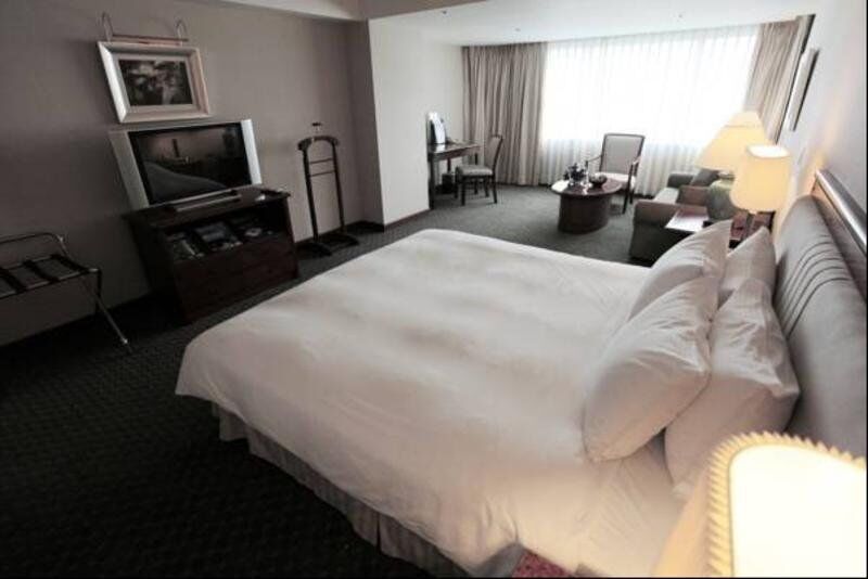 Evergreen Laurel Hotel - Tchaj-čung Exteriér fotografie The photo shows a hotel room featuring a large bed with white bedding. There is a flat-screen television on a wooden cabinet opposite the bed. Nearby, there are two armchairs and a small table, creating a cozy seating area. Large windows allow natura