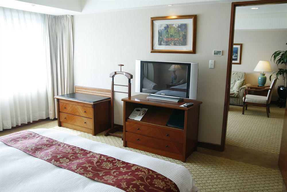 Evergreen Laurel Hotel - Tchaj-čung Exteriér fotografie The photo depicts a hotel room interior. In the foreground, there is a neatly made bed with a decorative red bedspread. To the left, a large window allows natural light to fill the room, with light-colored curtains drawn to one side. 

Next to the be